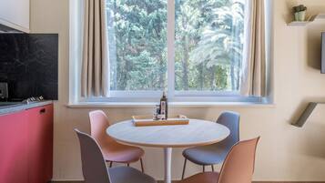 A dining area with a round table, four chairs, a kitchen with a red cabinet, and a window with curtains.