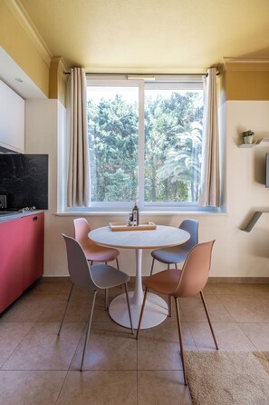 A dining area with a round table, four chairs, a kitchen with a red cabinet, and a window with curtains. - Résidence Château d'Acotz (Saint-Jean-de-Luz)