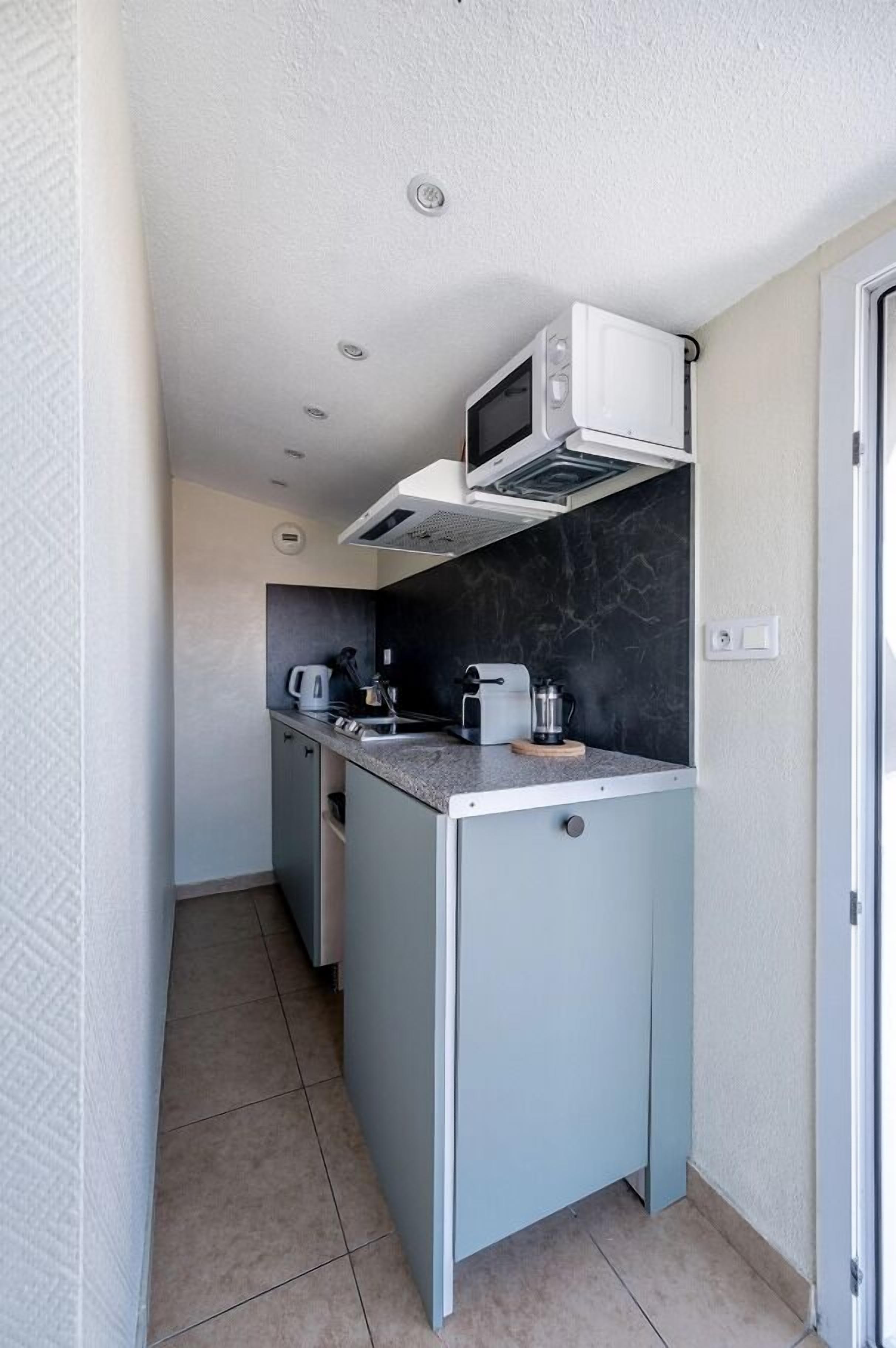 Cocina compacta con microondas, tostadora y cafetera en la encimera, un lavabo pequeño y un armario.