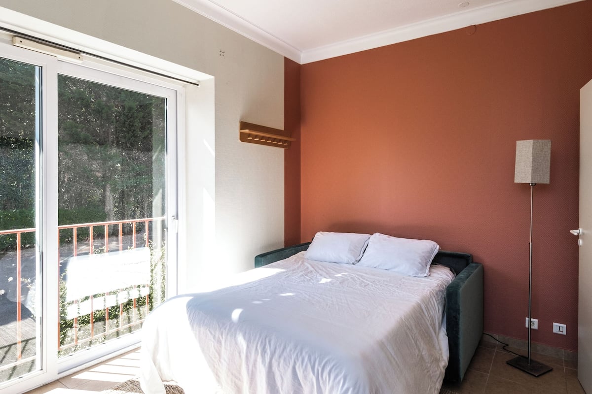 Un dormitorio con cama, lámpara de techo, lámpara de pie y puerta corrediza de vidrio que da a un área exterior.