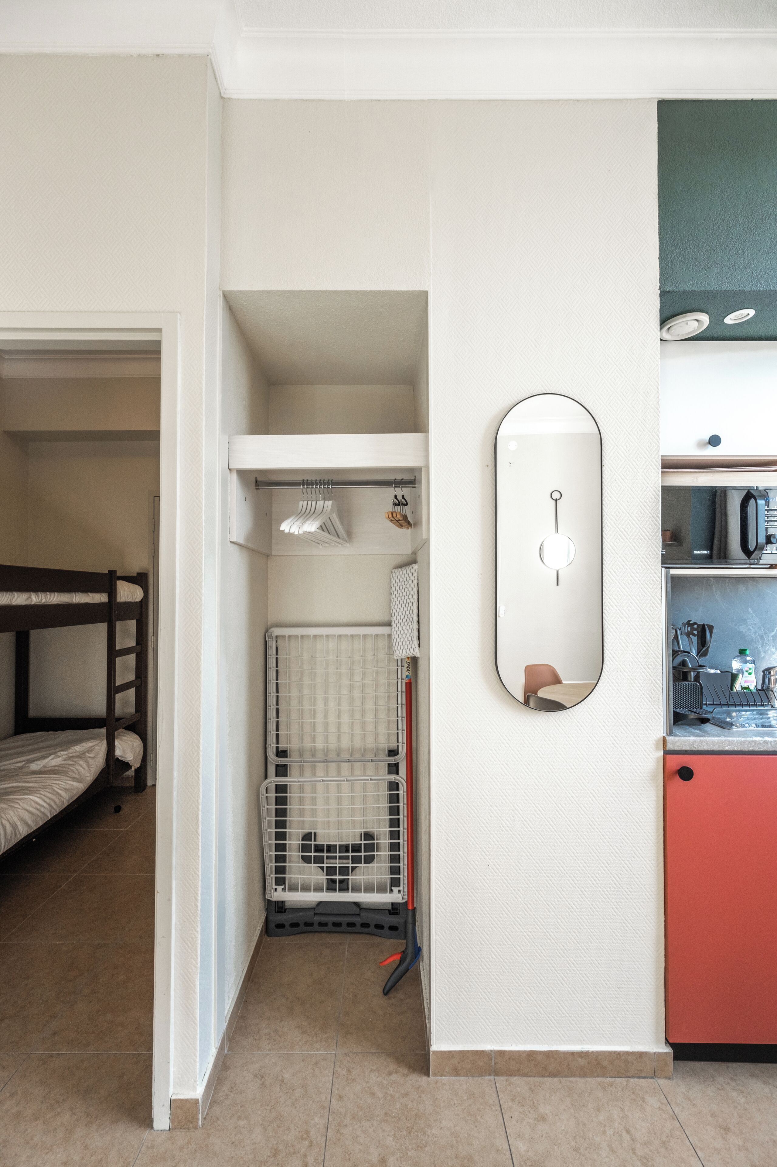 Habitación pequeña con una cama litera, una kitchenette, un espejo y una jaula para mascotas.