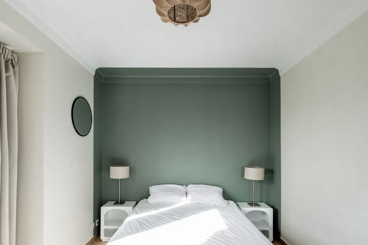 Un dormitorio con una cama, dos mesitas de noche, una lámpara colgante y un reloj de pared.