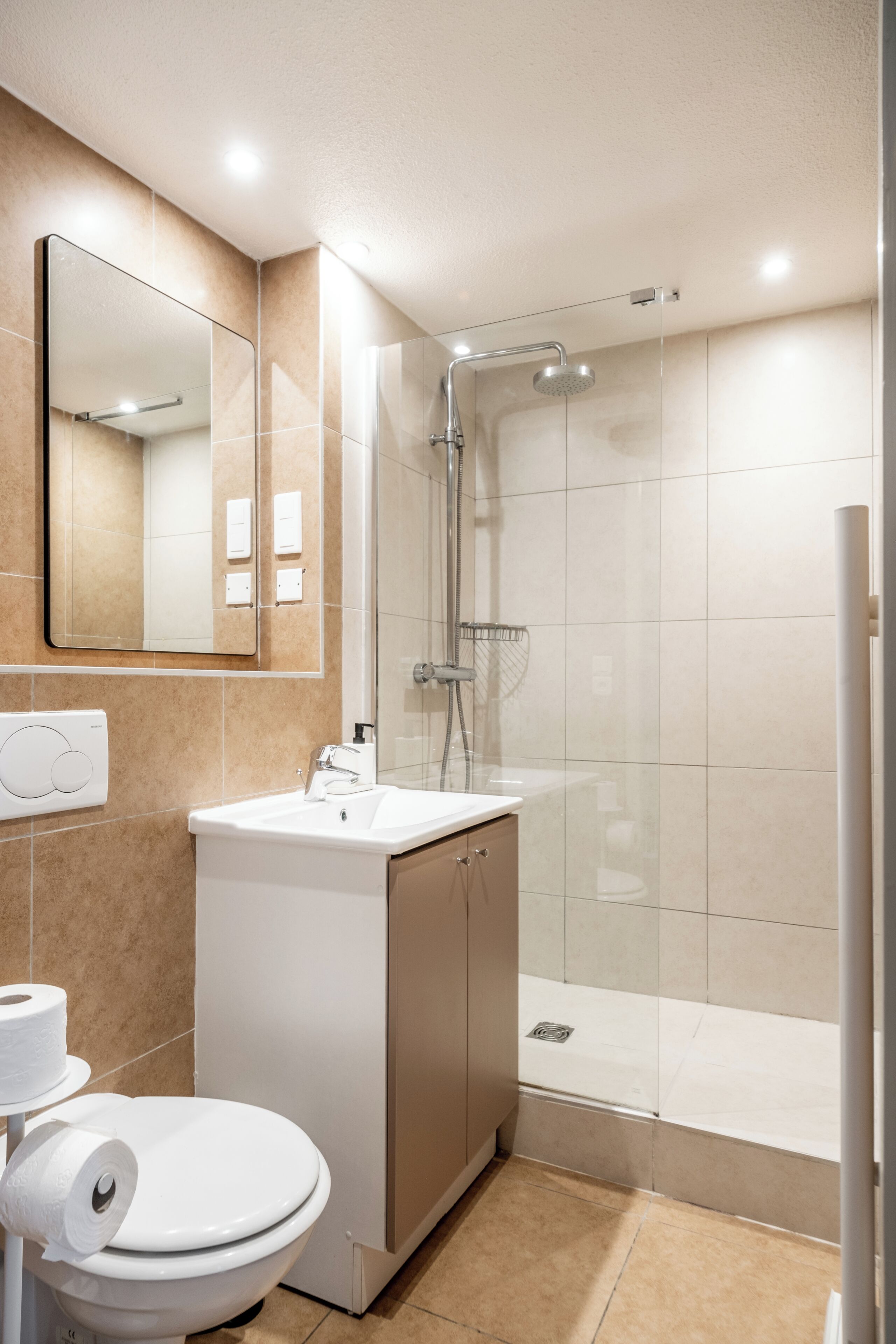 A modern bathroom with a toilet, sink, mirror, shower, and tiled walls.