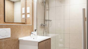 A modern bathroom with a toilet, sink, mirror, shower, and tiled walls.