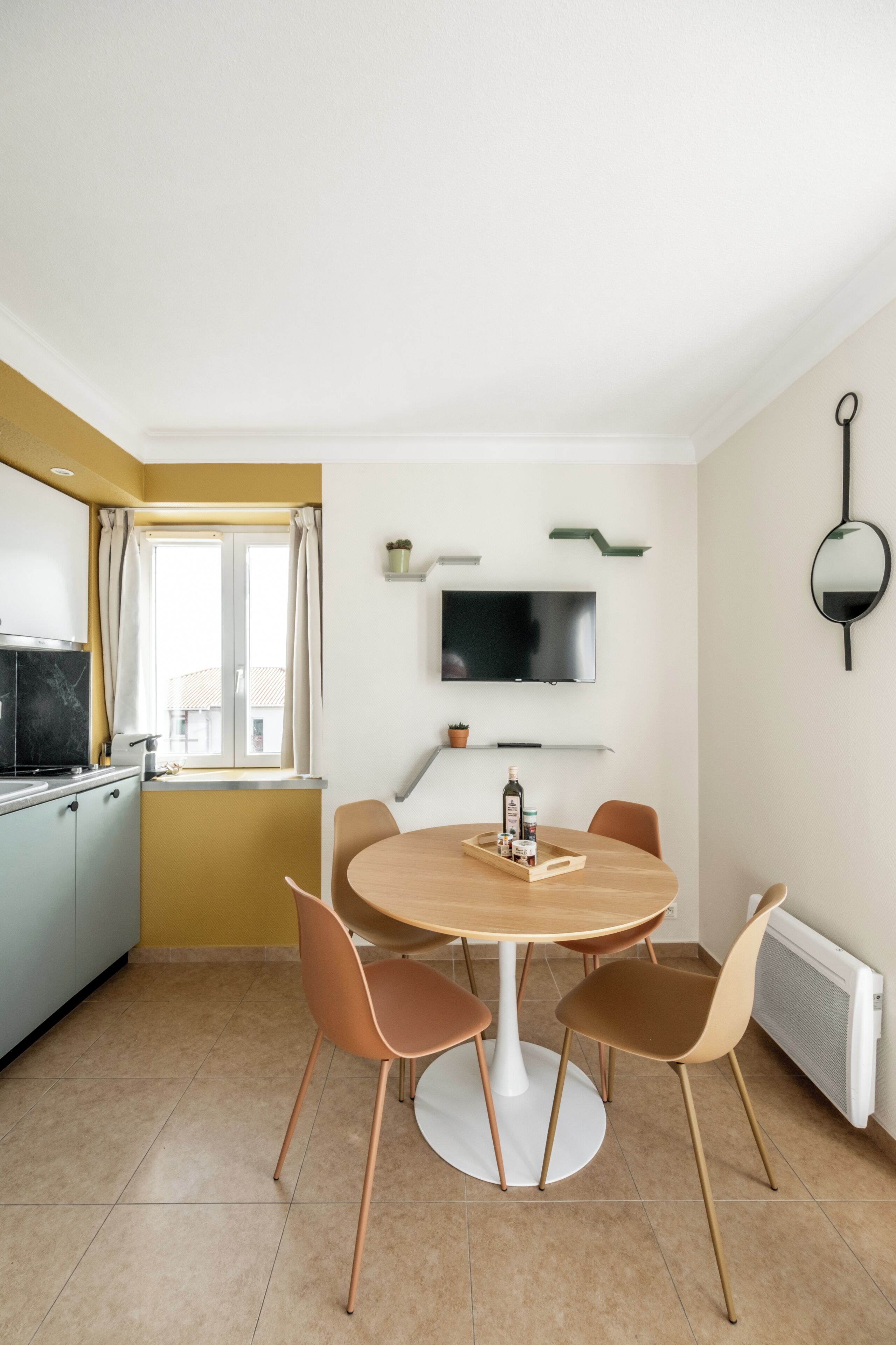 A modern kitchen with a dining area, a flat-screen TV, and a window with curtains.