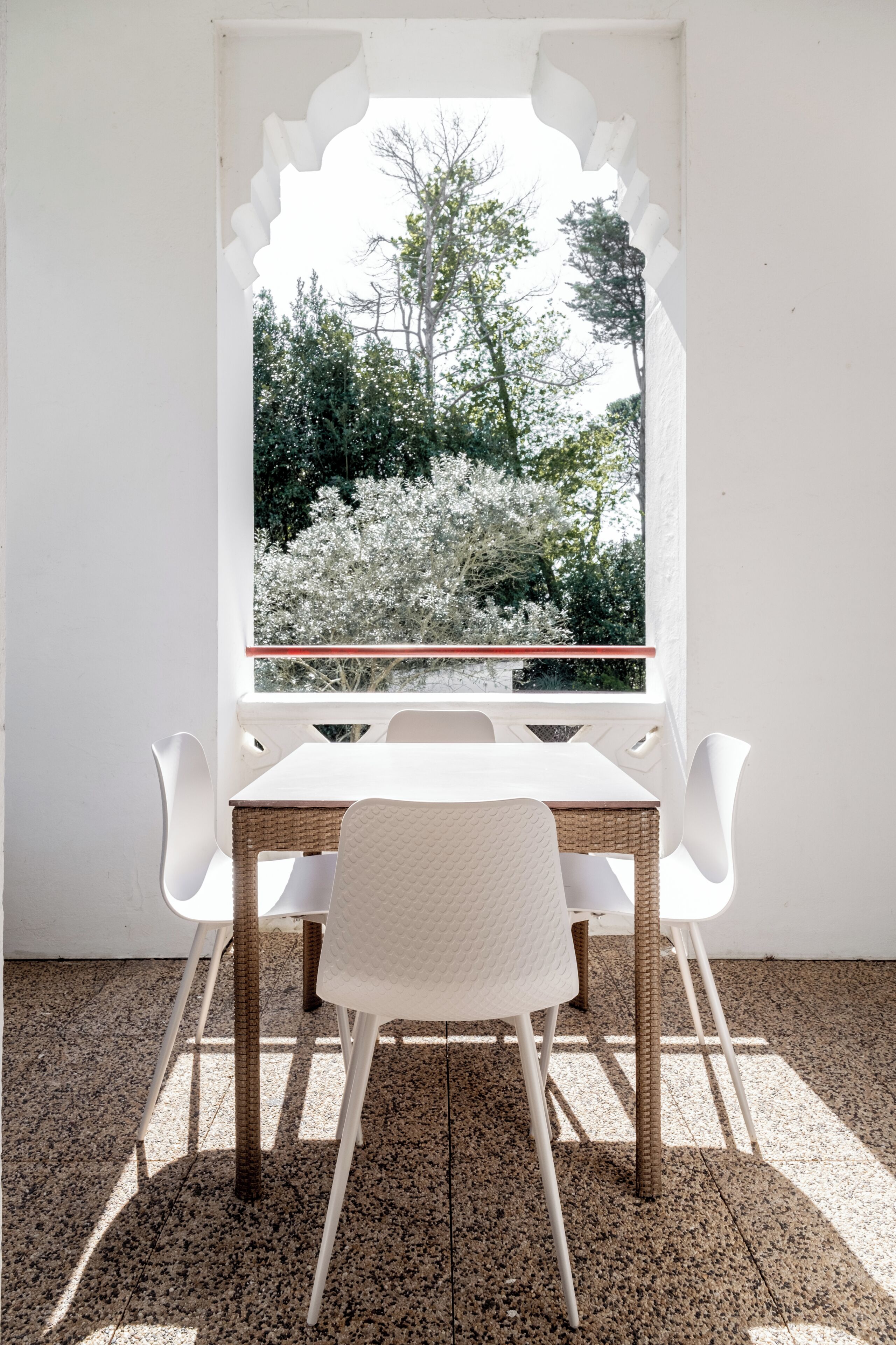 A dining area with a table and chairs, a window with a view of trees, and a tiled floor.