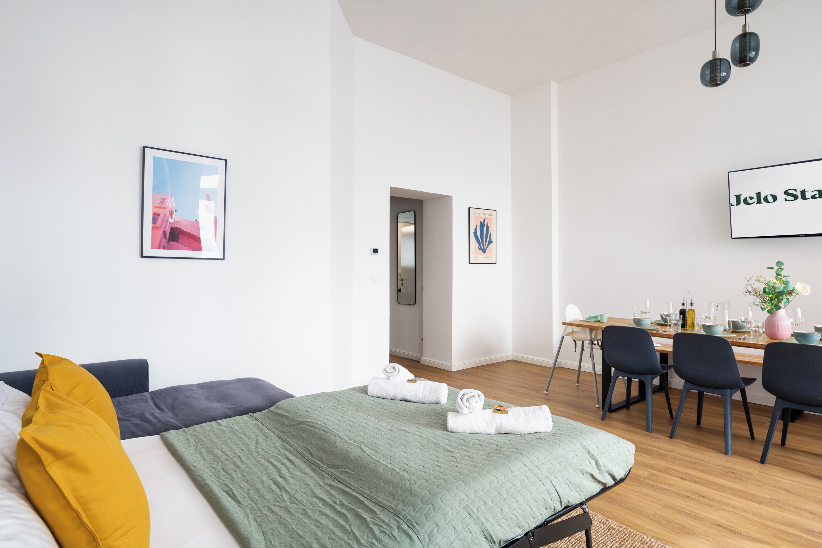 A modern hotel room with a bed, a desk, and a dining area.