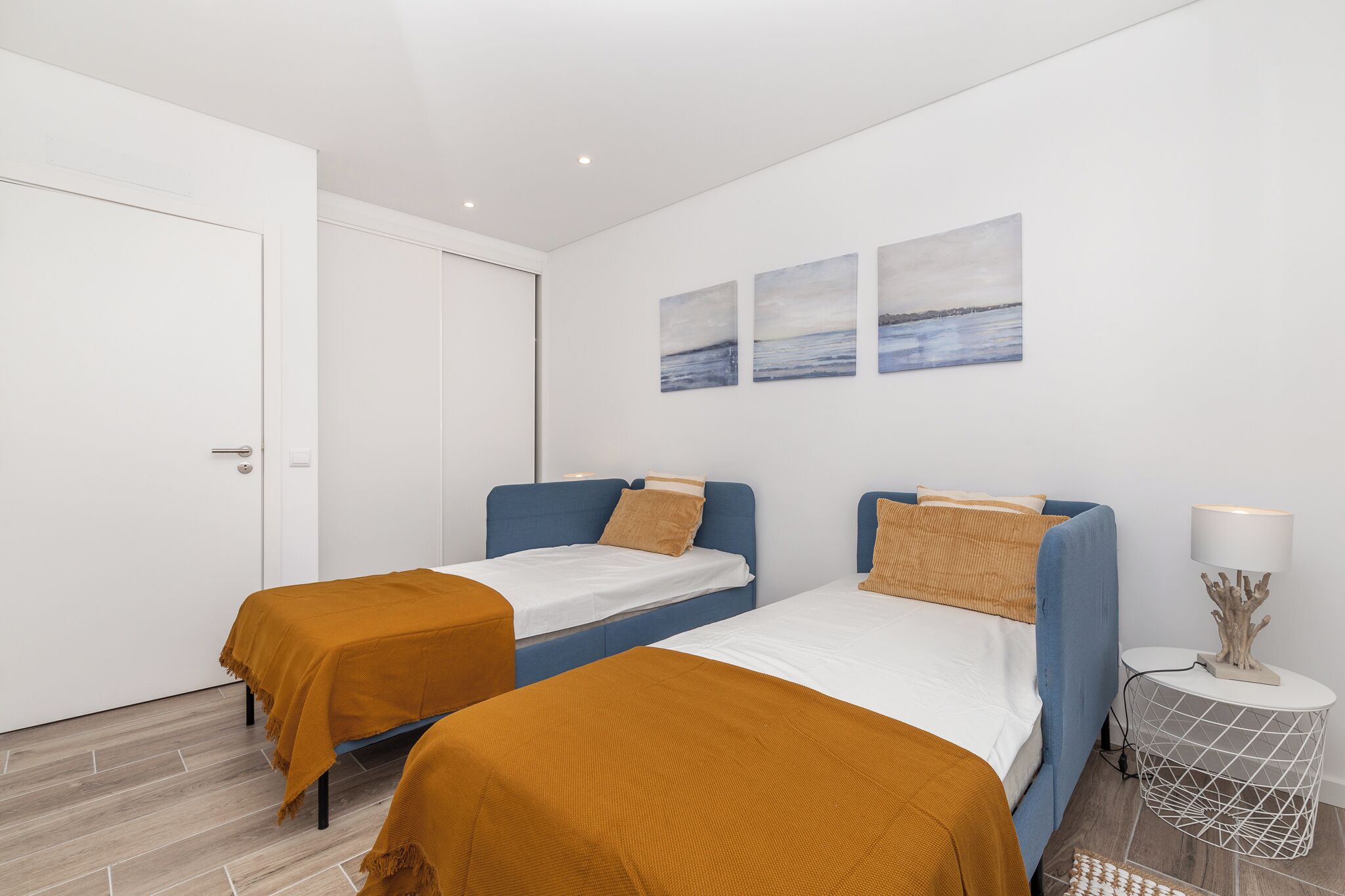 Una habitación de hotel moderna con dos camas individuales, una puerta blanca y tres cuadros colgados en la pared.