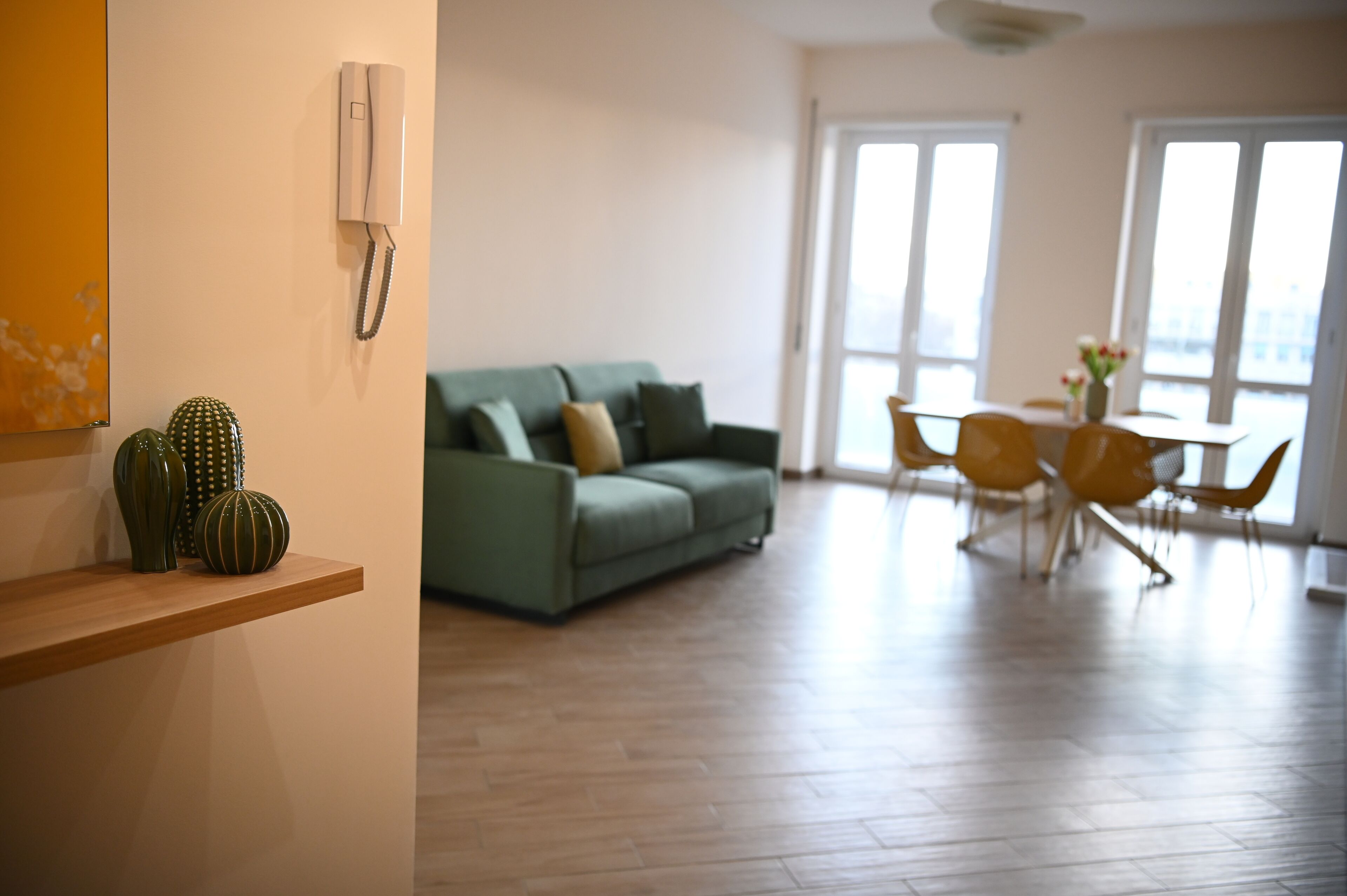 A modern living room with a green sofa, wooden flooring, and a dining area with yellow chairs.