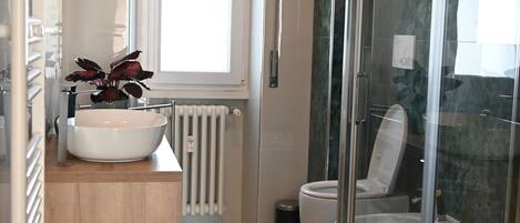 Une salle de bain moderne dotée d’une grande fenêtre, d’un lavabo blanc et d’une cabine de douche en verre.