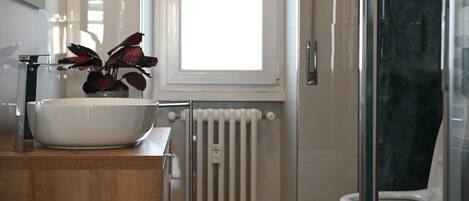 A modern bathroom with a large white sink, a wooden vanity, a glass shower enclosure, and a radiator.