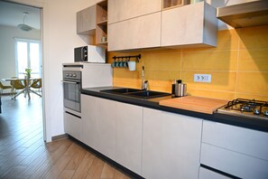 Une cuisine moderne avec des meubles blancs, un plan de travail noir, une cuisinière à gaz et un évier.