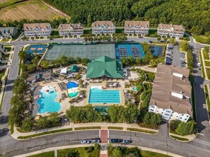 Vista aérea de un área residencial con varias casas, una cancha de tenis y un complejo de piscinas.
