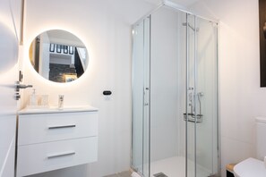 A modern bathroom with a glass-enclosed shower, a round mirror with integrated lighting, and a white vanity with drawers. - Luxury Villa Libellile (San Miguel de Abona)