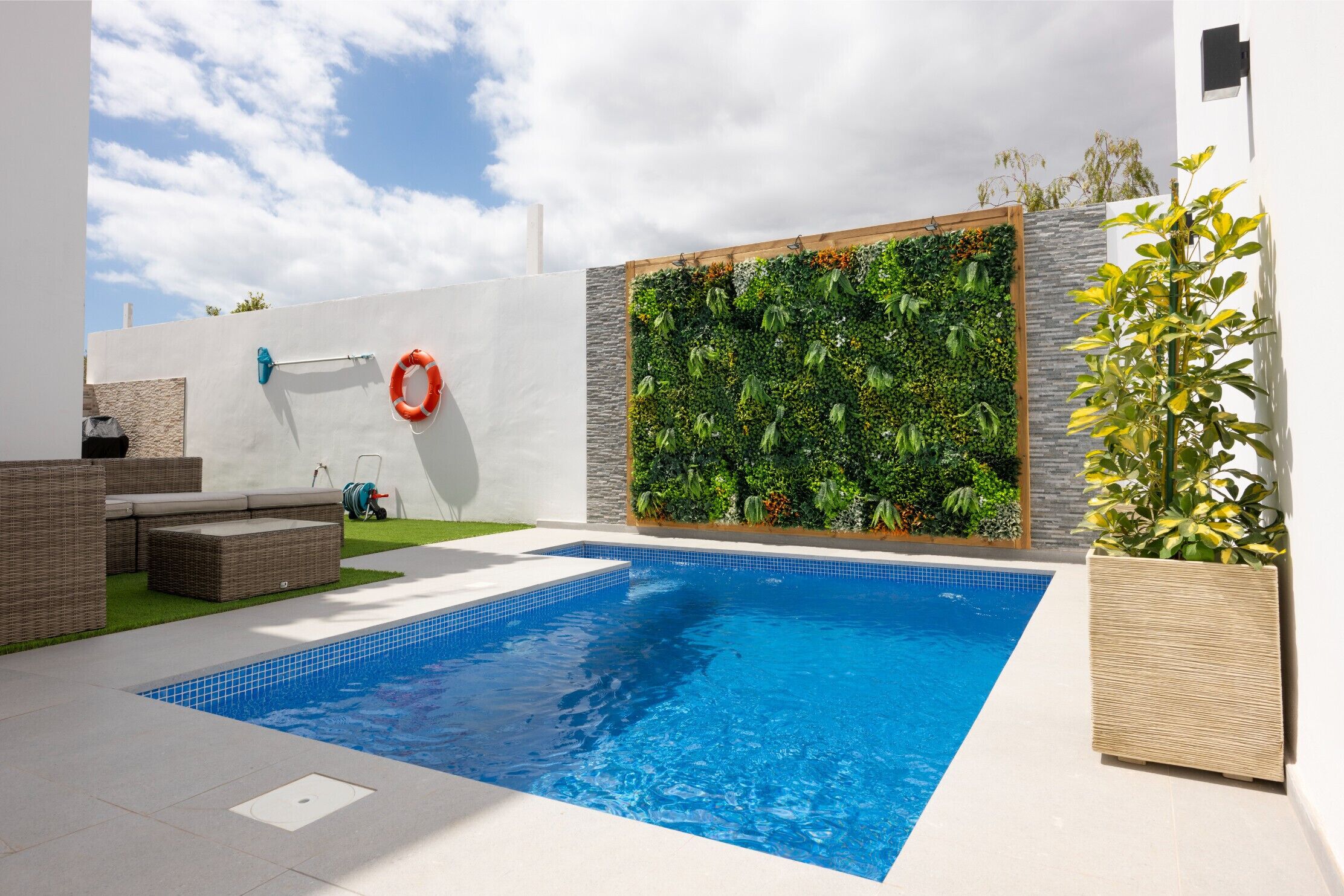 Una piscina con borde de azulejos, rodeada por un muro blanco y un jardín vertical.