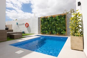 A swimming pool with a tiled edge, surrounded by a white wall and a vertical garden. - Luxury Villa Libellile (San Miguel de Abona)