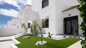 A modern white building with a flat roof, a small garden with palm trees, and a clear blue sky.