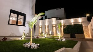 A modern building with a well-lit outdoor area featuring a lawn, seating, and decorative plants.