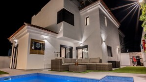 A modern house with a swimming pool, outdoor seating, and a well-lit patio area.