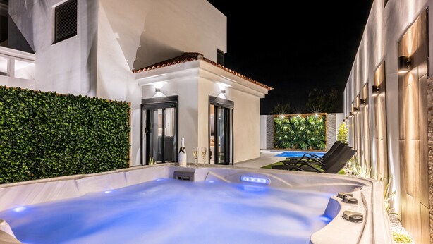 A hot tub with a tiled surround, a pool, and a well-maintained hedge.