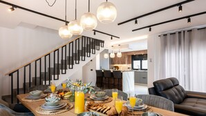 A dining area with a wooden table set for breakfast, a staircase, and a modern kitchen in the background.
