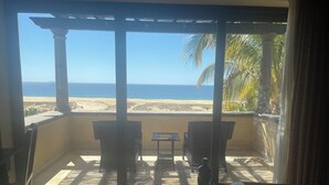 A balcony with a view of the beach, two chairs, a small table, and a sofa. - Vicroy Novaispania Estates (Cabo San Lucas)