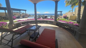 A covered outdoor seating area with a view of the ocean, featuring a pool, palm trees, and vibrant flowers. - Vicroy Novaispania Estates (Cabo San Lucas)