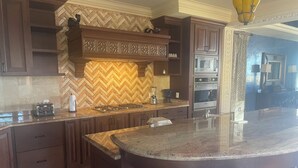 A kitchen with dark wooden cabinets, a herringbone tile backsplash, a central island, and built-in appliances including a stove, microwave, and oven. - Vicroy Novaispania Estates (Cabo San Lucas)