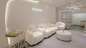 A modern hotel lobby with a white sofa, a round ottoman, and a cart with snacks. - At Home Hotel NanShi (Taipei)