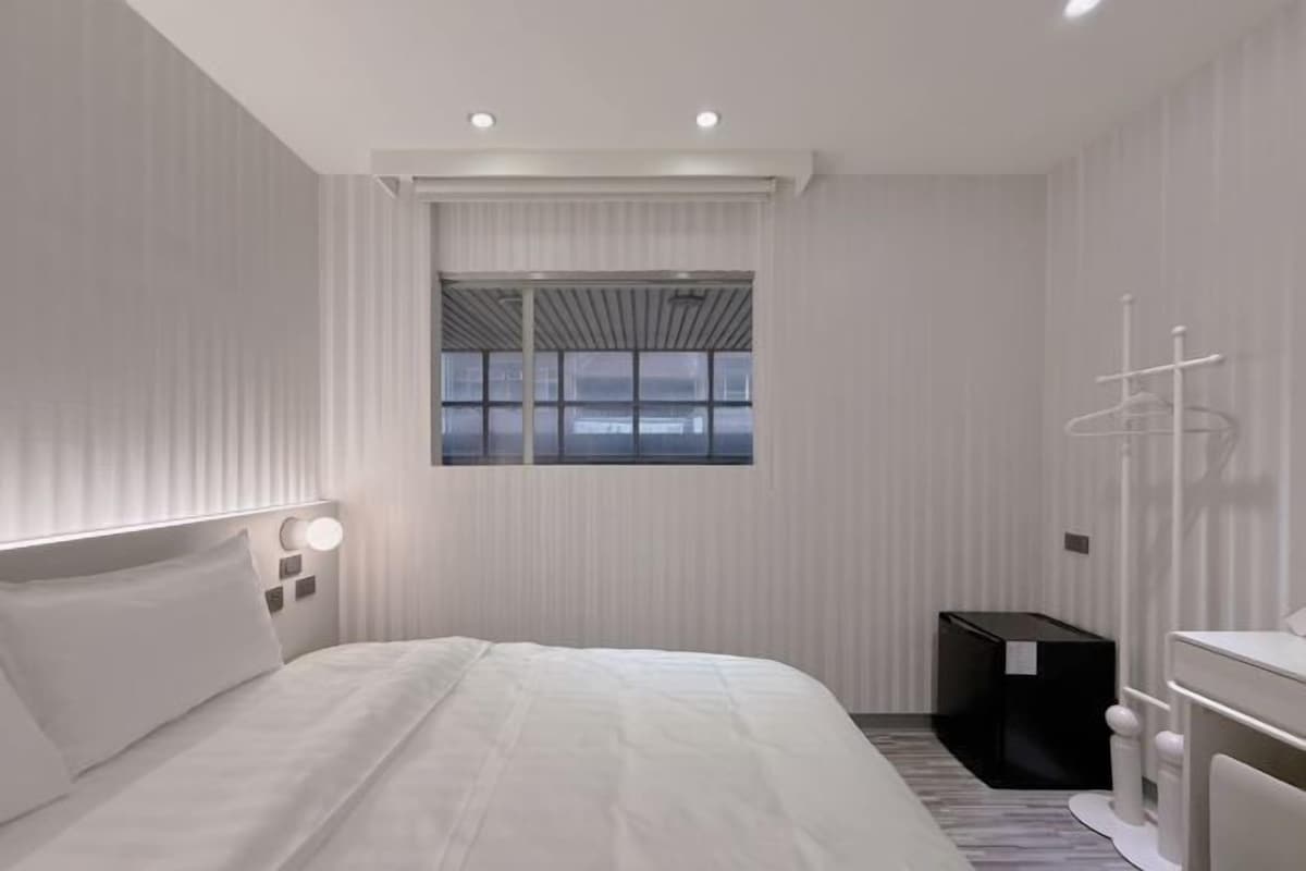 Una habitación de hotel moderna con una cama grande, una mesita de noche, una ventana y un armario.