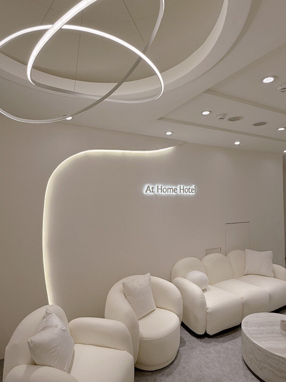 Una moderna hall d'albergo con una reception dalla forma curva, una zona salotto e un tavolino rotondo.