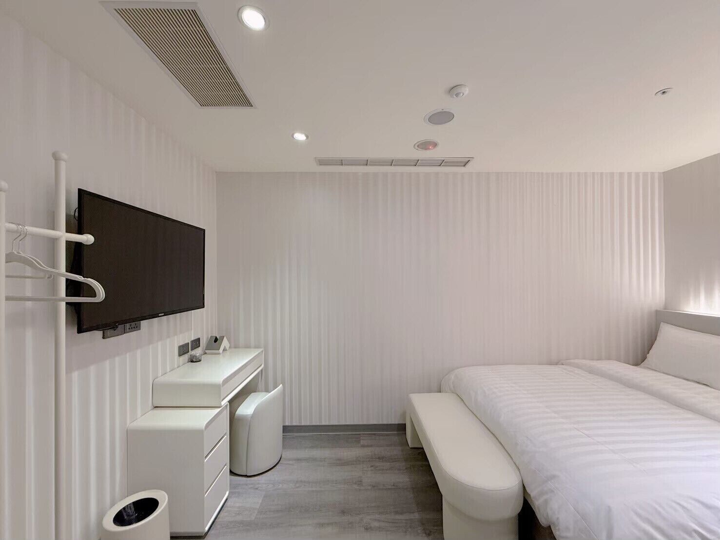 A modern bedroom with a large bed, a TV mounted on the wall, a bedside table, and a small white dresser.
