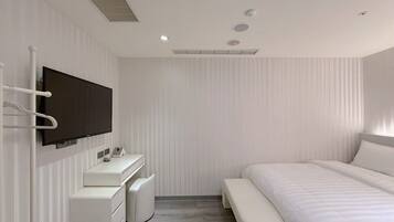 A modern bedroom with a large bed, a TV mounted on the wall, a bedside table, and a small white dresser.