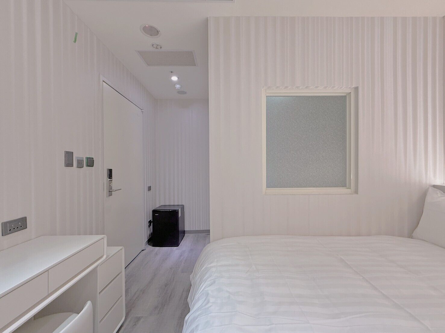 A modern bedroom with a large bed, a bedside table, a wardrobe, a desk, and a small black cabinet.