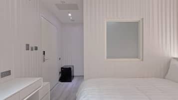 A modern bedroom with a large bed, a bedside table, a wardrobe, a desk, and a small black cabinet.