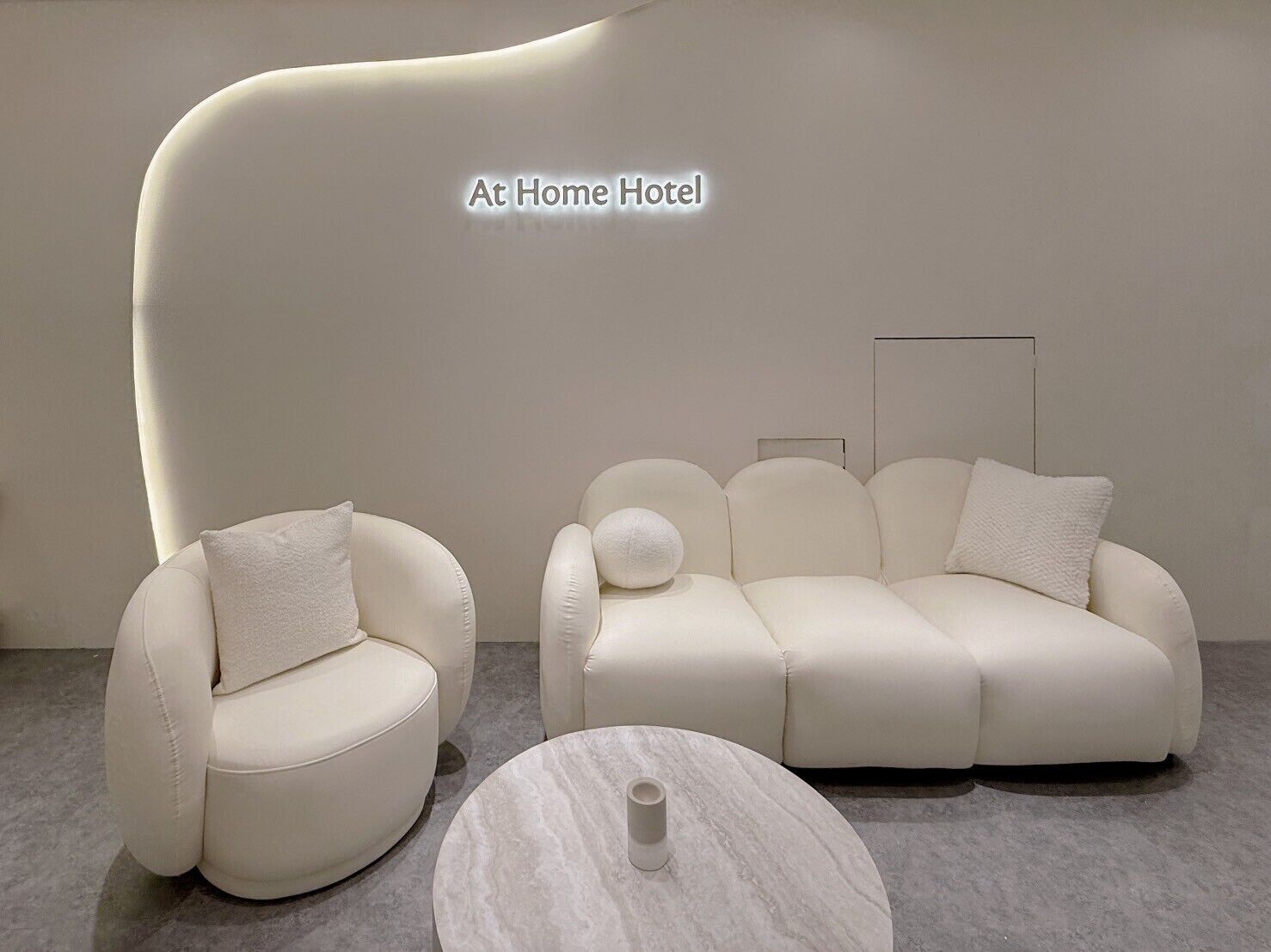 A modern hotel room with a white sofa, a smaller armchair, and a marble coffee table.