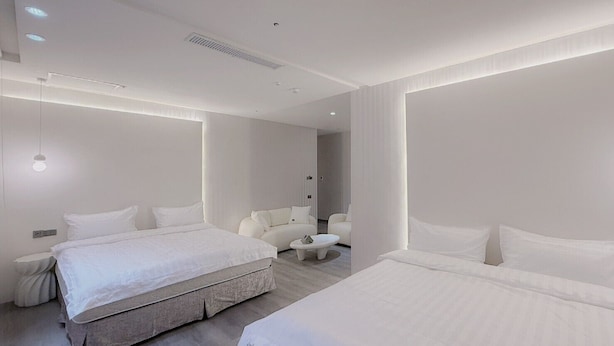 A modern hotel room with a large bed, a smaller bed, two chairs, and a small table. - At Home Hotel NanShi (Taipei)