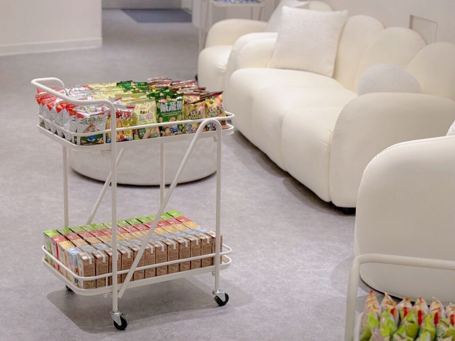 A white sofa in a modern living room with a white metal cart filled with packaged goods.