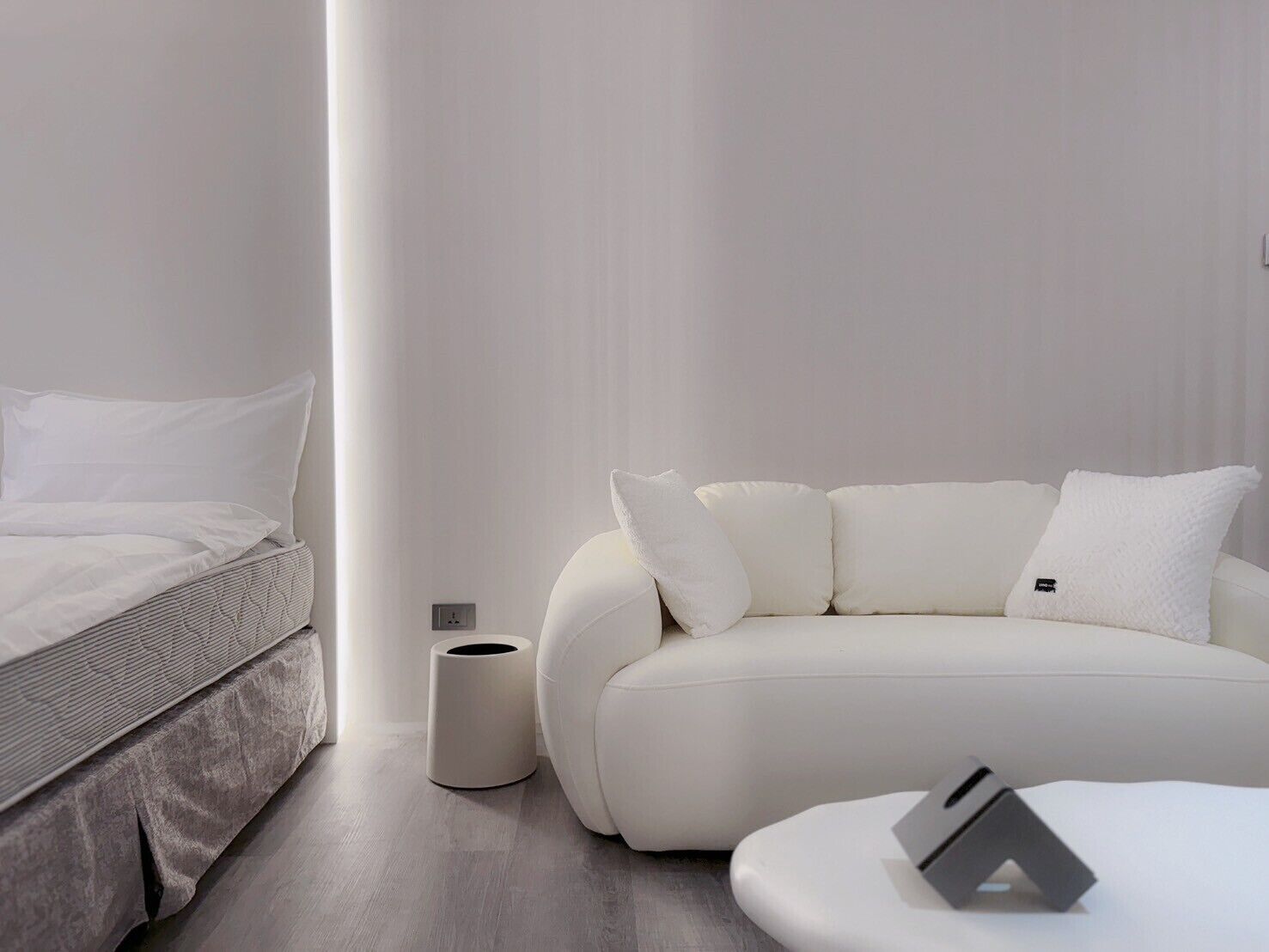 A modern, minimalist bedroom with a bed, a white sofa, and a small table.