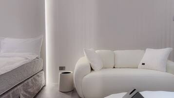 A modern, minimalist bedroom with a bed, a white sofa, and a small table.