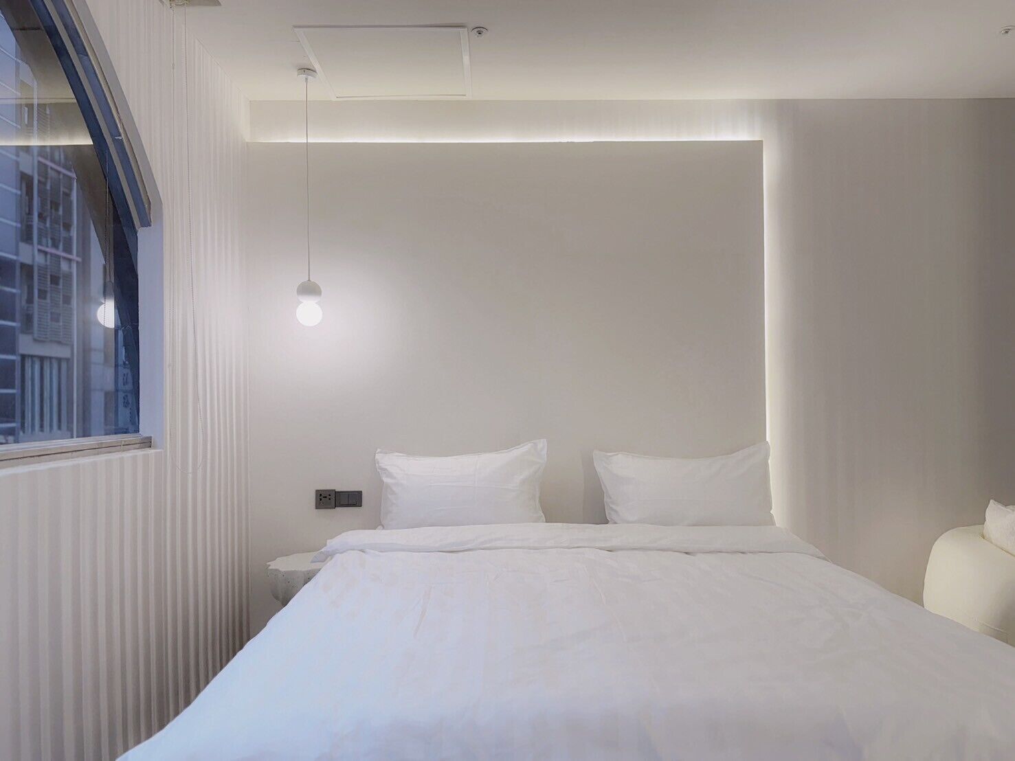 Et minimalistisk hotelværelse med en stor seng, et natbord og et vindue med persienner.