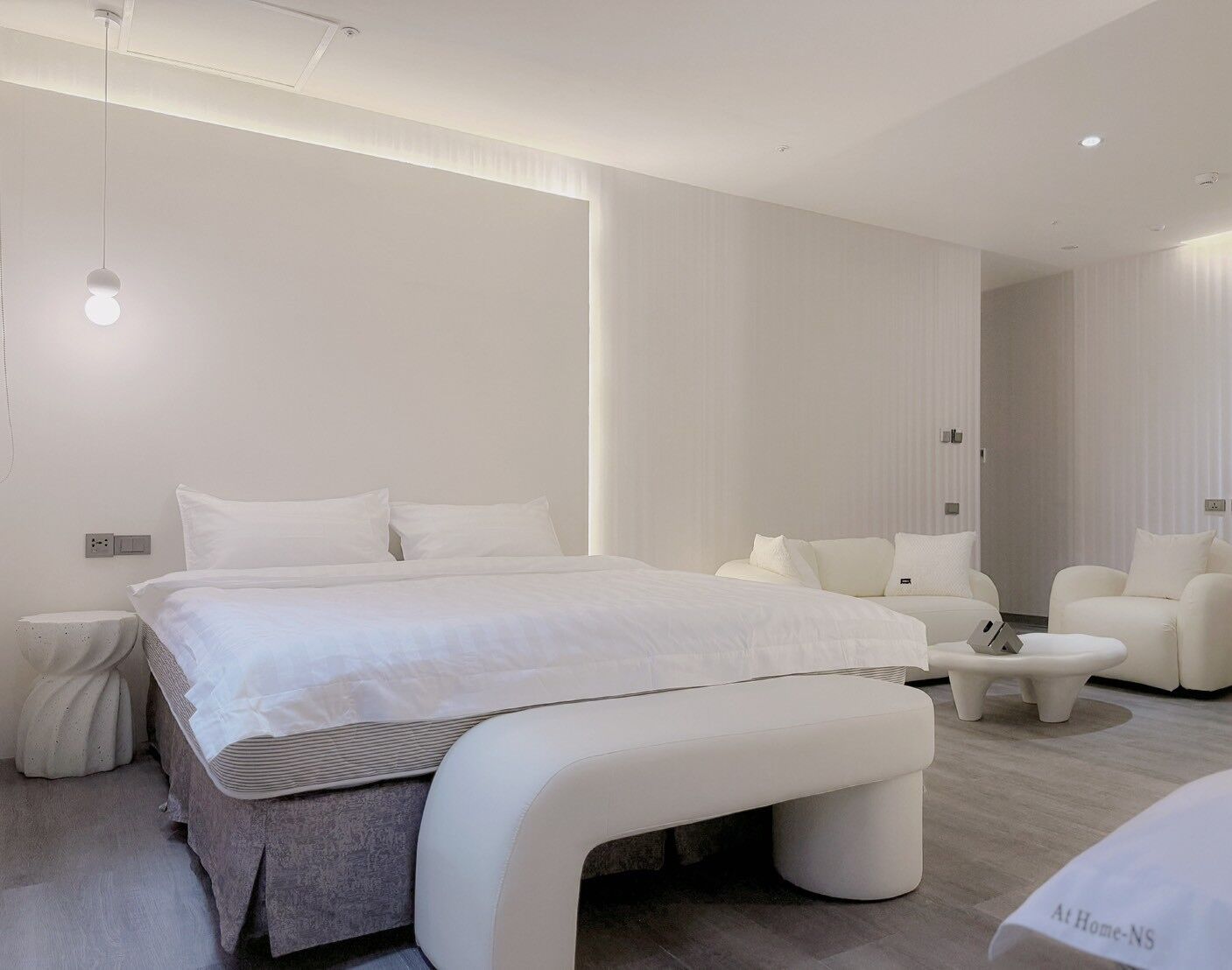 A modern bedroom with a large bed, a bedside table, a bench, and a seating area with a sofa and armchairs.