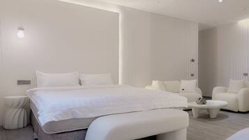 A modern bedroom with a large bed, a bedside table, a bench, and a seating area with a sofa and armchairs.
