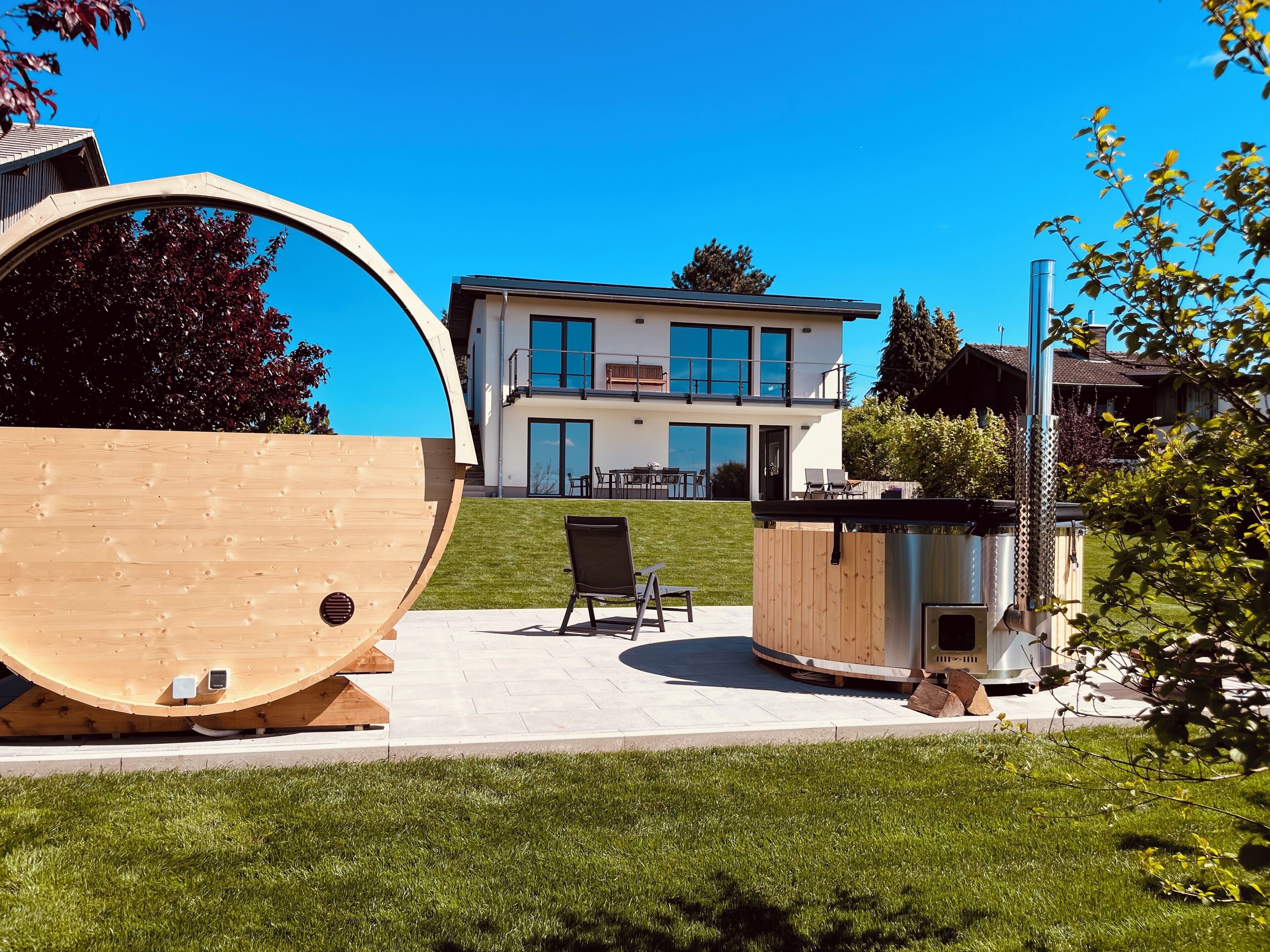 Una casa moderna de dos pisos con un amplio balcón, una parrilla y un barril de madera.