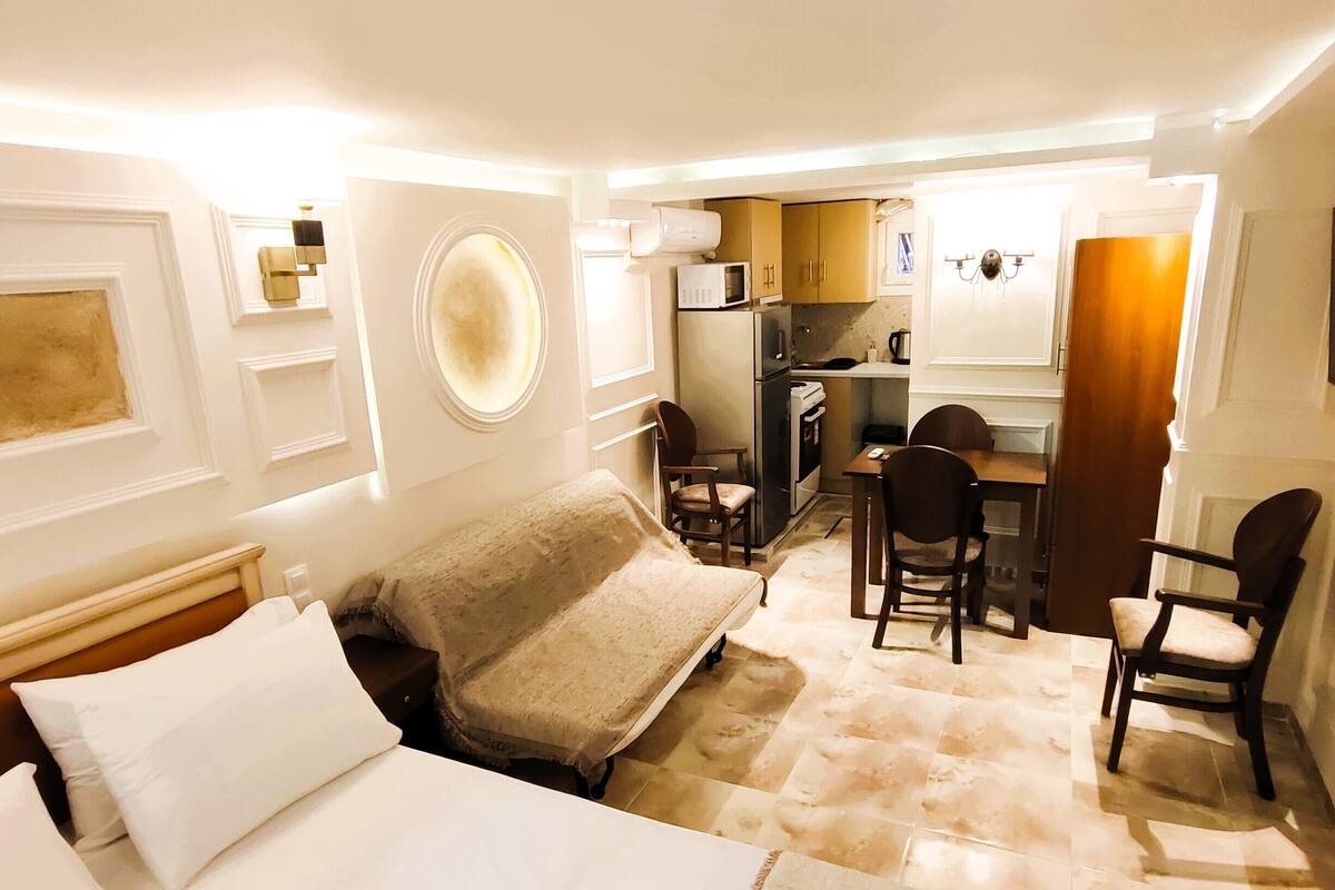 A compact hotel room with a bed, a small kitchenette, and a seating area.