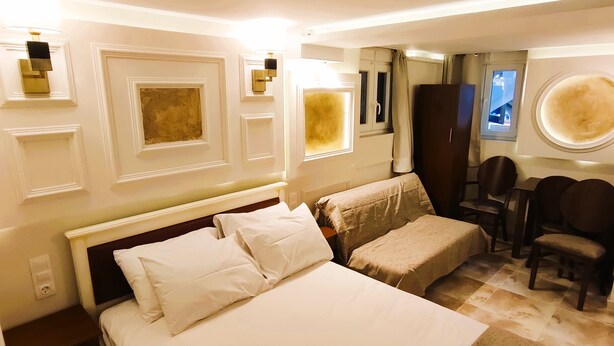 A hotel room with a large bed, a small table, and a chair. There are wall sconces and a window with curtains. - Villa Miltiadis GreeceFiloxenia (Volos)