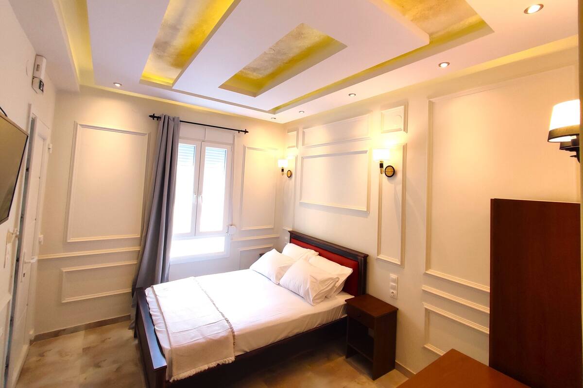 A hotel room with a bed, bedside table, and a window with curtains.