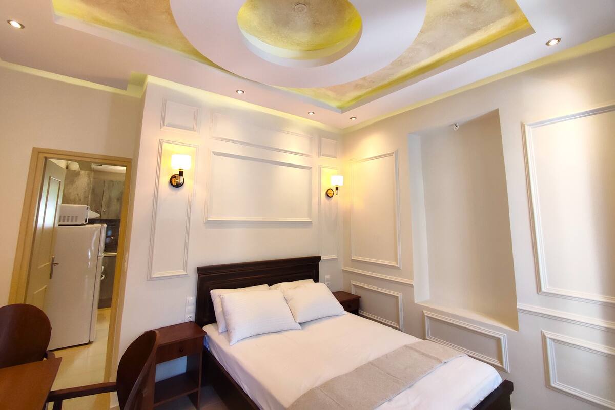 A hotel room with a bed, bedside tables, a desk, and a mirror.