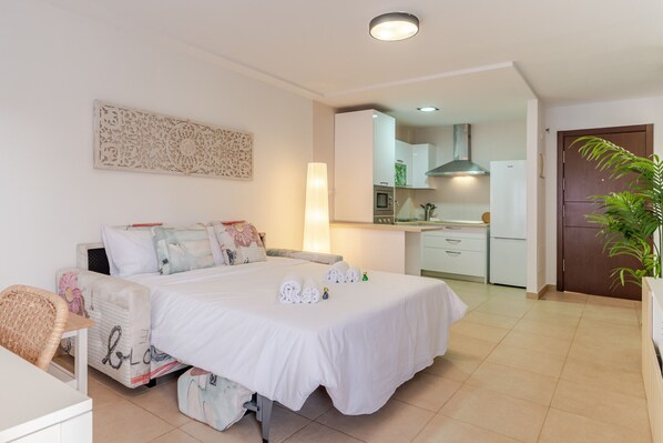 Une chambre moderne avec un grand lit, une table de chevet, une chaise et une vue sur la cuisine.