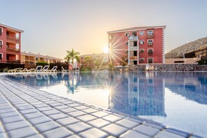 Une piscine avec des chaises longues, un bâtiment rouge doté de balcons et un ciel dégagé.